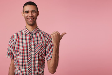 studio portrait of middle age middle eastern man wears blue shirt points aside with positive, happy facial expression isolated over pink background