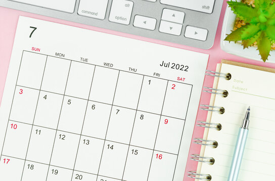 July 2022 calendar sheet with keyboard computer on pink background.
