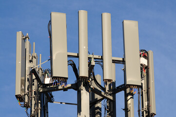 A close-up view of a modern cellular communication tower equipped with multiple antennas and cables...