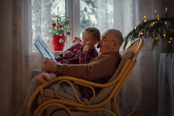 grandfather sitting in a chair and reading a fairy tale to his granddaughter on Christmas eve