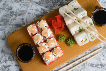 Delicious sushi rolls with chicken, cheese, shrimp, red ginger, wasabi and soy sauce on a wooden board on a light background with copy space