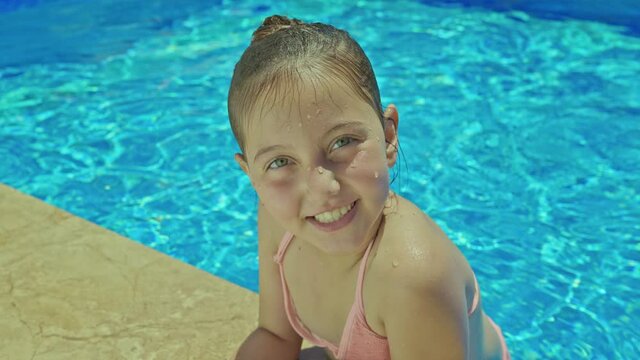 A little girl is having fun in the pool.Little girl in pink swimsuit swimming in pool and smiling at camera waving at camera.