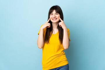 Obraz na płótnie Canvas Teenager Ukrainian girl isolated on blue background smiling with a happy and pleasant expression