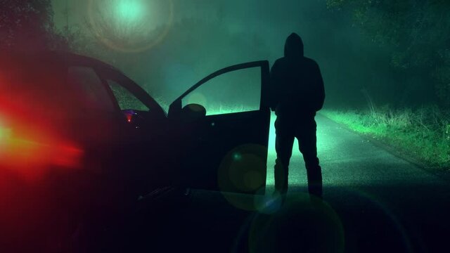 A science fiction concept of a man next to a car looking at a UFO floating above a road. On a scary forest road at night.