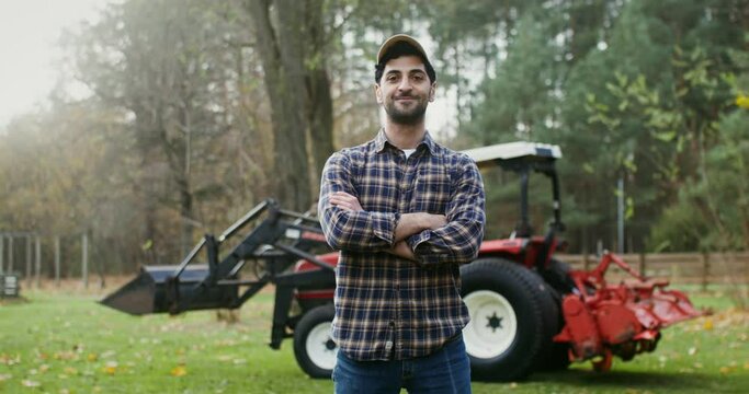 Young farmer smiling looking straight into the camera stands near tractor