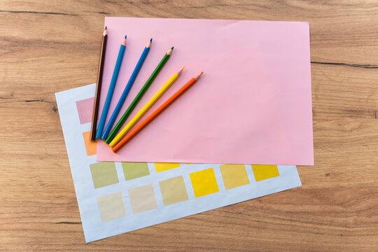 Six color pencils laying at the wooden table with pink paper and palette of colors. Back to school or designer workplace concept. Stock photo
