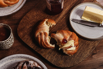Freshly baked cardamom knot buns (also sweet rolls or swirl buns) with cocoa mug and butter and jam on wooden table. Cosy winter breakfast. Selective focus