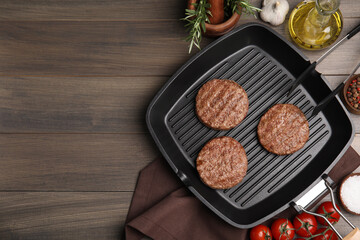 Grill pan with tasty fried hamburger patties and seasonings on wooden table, flat lay. Space for...