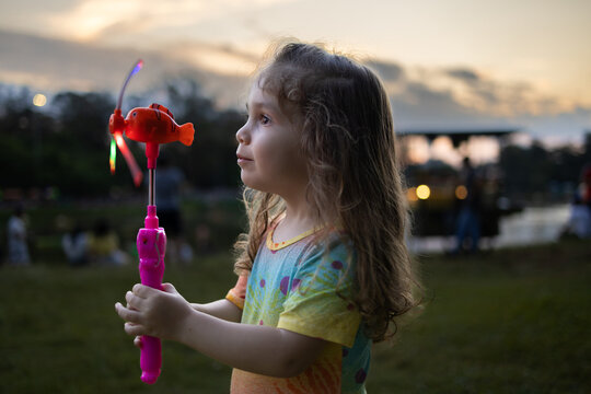 garotinha de 2 anos, usando roupa colorida e brincando com seu catavento colorido em parque publico 