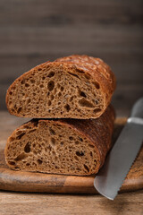 Cut rye baguette with knife on wooden table, closeup