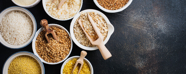 Variety of cereal flakes rice, millet, buckwheat, oatmeal. Superfood in white ceramic bowls on dark old concrete background. Top view.