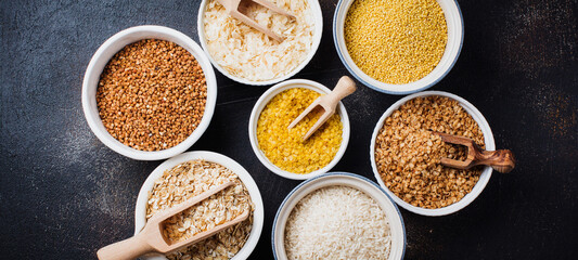 Variety of cereal flakes rice, millet, buckwheat, oatmeal. Superfood in white ceramic bowls on dark old concrete background. Top view.