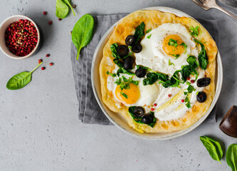 Turkish eggs flatbread with yoghurt, cheese, olives, spinach and red pepper on ceramic vintage plate on gray old background. Top view.
