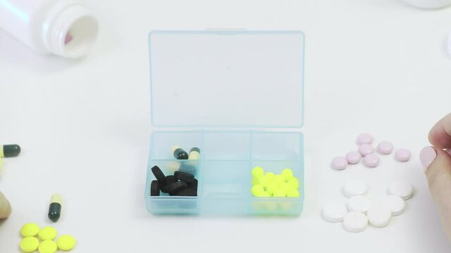 Close-up of a pillbox with different tablets. A person's hands put pills in a pillbox