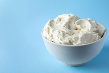 Bowl of tasty cream cheese on light blue background, space for text