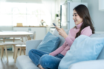 Asian beautiful woman sit on sofa and chat on mobile phone in house. 