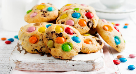 Stack of children's cookies with colorful chocolate candies in a sugar glaze on a white light wooden background. Selective focus