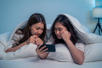 Asian attractive lesbian couple use mobile phone watch movie on bed.