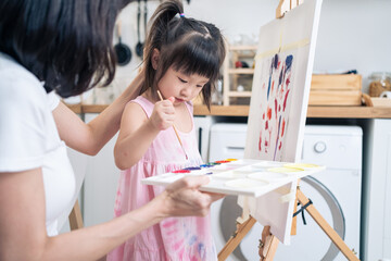 Asian young happy kid daughter coloring on painting board with mother. 