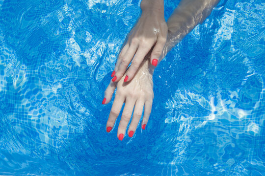 Image of woman's hands with red nail polish in blue water