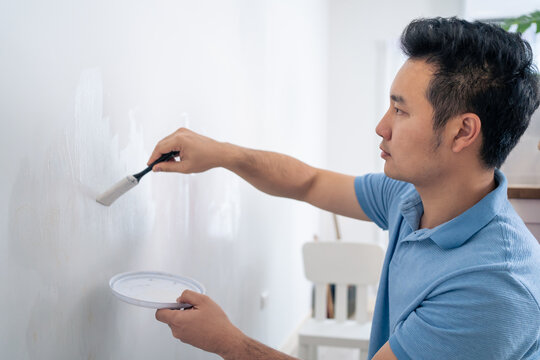 Asian attractive man paint white wall with brush to repair living room