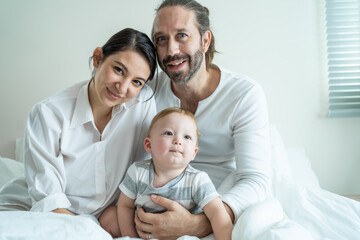 Portrait of Caucasian happy family smiling, look at camera in bedroom.