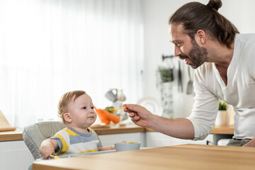 Obraz na płótnie Canvas Caucasian beautiful father take care of baby boy toddler in kitchen.