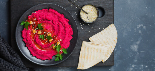 Homemade beetroot hummus in black ceramic dish on old dark concrete background. Selective focus. Top view.