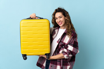 Young caucasian woman isolated on blue background in vacation with travel suitcase