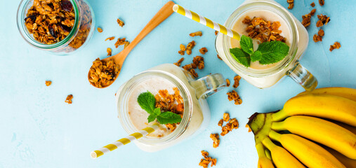 Banana smoothie with granola, dried fruits and mint on gray concrete background. Top view