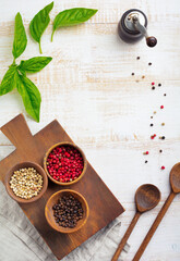 Red, white and black peppers, basil leaves, simple old spoons and linen napkin on old wooden stand. Kitchen accessory concept. Selective focus. Top view. Toned image