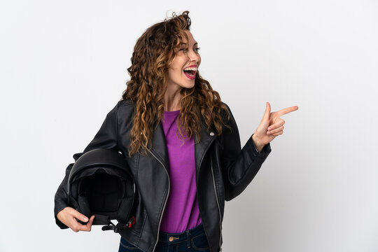 Young caucasian woman holding a motorcycle helmet pointing finger to the side and presenting a product