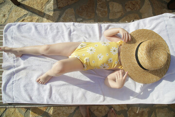 Toddler girl laying on sun bed and hiding from sun under straw hat. Happy summer time childhood...