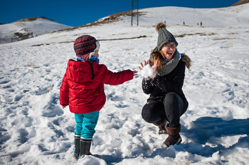 Un niño le tira una bola de nieve a su madre que rie 