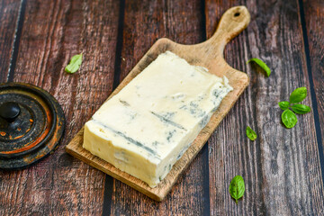 Gorgonzola cheese on cutting board with fresh  basil . Veined Italian  blue cheese.