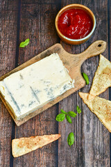 Gorgonzola cheese on cutting board with fresh  basil  and  home made crispy nachos  with spicy red sauce. Veined Italian  blue cheese. 