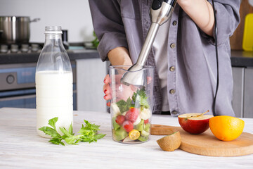 Woman using hand blender to make smoothies. Grey kitchen interior design. Vegetarian, clean eating...