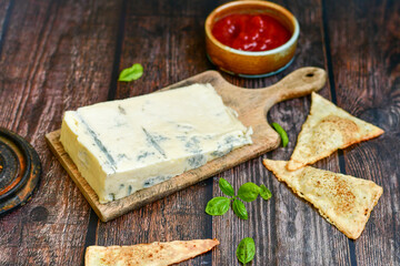 Gorgonzola cheese on cutting board with fresh  basil  and  home made crispy nachos  with spicy red sauce. Veined Italian  blue cheese. 
