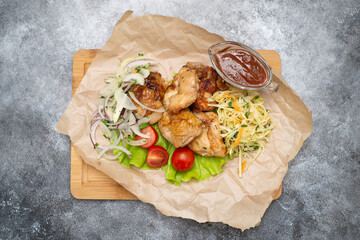 Griled chiken with tomatoes and green letuce salad, cabbage salad and red onion on the parchment paper and wooden.