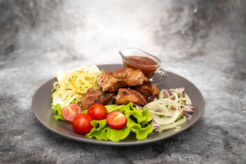 Grilled pork with tomatoes and green letuce salad, cabbage salad and red onion on the plate. top view. Grey background.