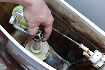 The plumber hand repair the sanitary equipment in old dirty empty drain water tank closeup - DIY WC...