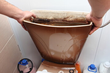 The plumber's white hands remove the old drain water tank from the toilet seat close up - DIY WC...