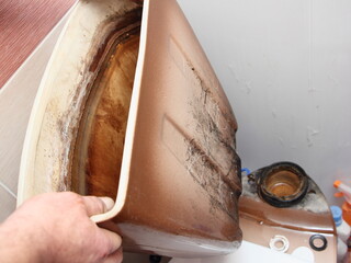 The plumber's hands remove the old dirty empty drain water tank with black mold closeup from the...