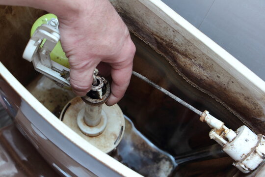 The plumber hand repair the sanitary equipment in old dirty empty drain water tank closeup - DIY WC service at home