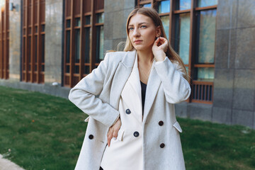 Serious independent female entrepreneur wearing white stylish suit standing with hand on waist in city and looking away with confidence  