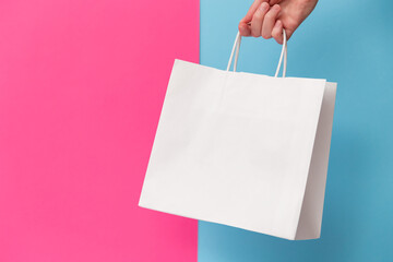 Female hand holding white blank shopping bag isolated on pink and blue background. Black friday...