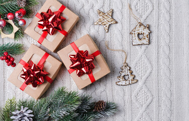 Warm cozy winter concept. Christmas tree branches, gifts in craft paper and ceramic Christmas decorations on a beige knitted background, copy space, selective focus