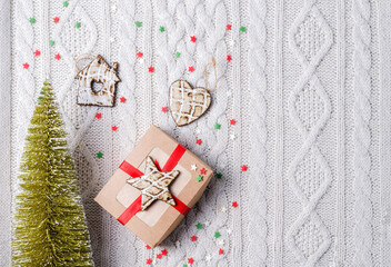 Warm cozy winter concept. Eco Christmas tree, gifts in kraft paper and ceramic Christmas decorations on a beige knitted background, copy space, selective focus