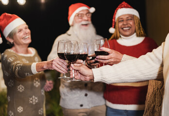 Elderly multiracial friends celebrate Christmas together while cheering with wine - Focus on the hands