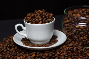 Fototapeta premium Coffee beans on a black background. A coffee cup full of coffee beans. Large serving of caffeine